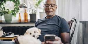 Senior man looking down at phone with a dog in his lap