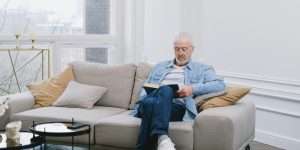Older man sat on couch at home reading a book