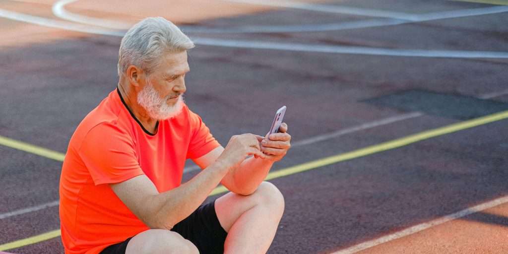 Senior man sat down on running track and looking at his phone