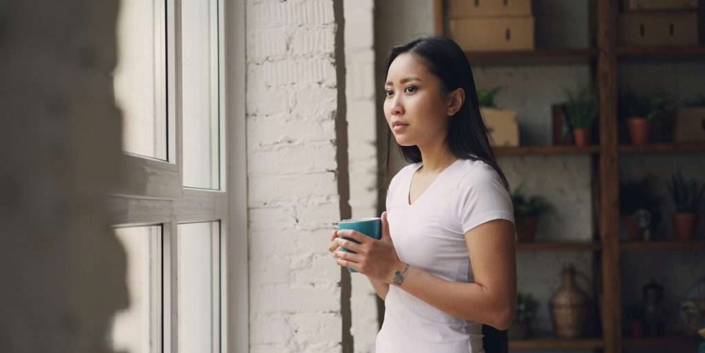 Young Woman Reflecting by Window Holding Mug
