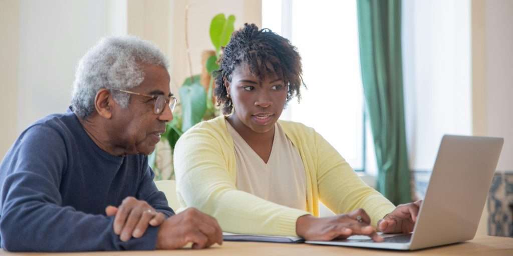 Senior man sitting with his adult daughter looking at a laptop screen at the table