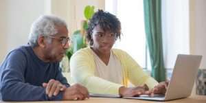 Senior man sitting with his adult daughter looking at a laptop screen at the table