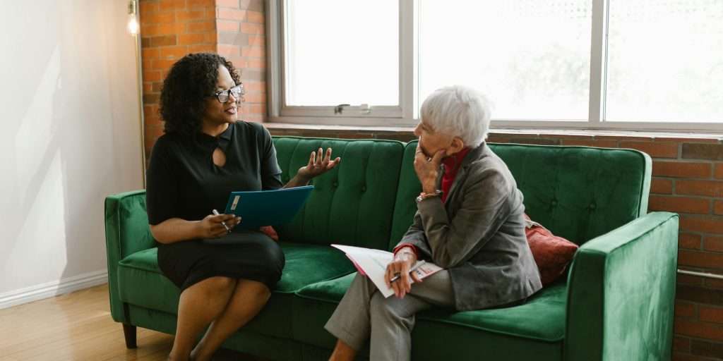 Two women engaged in a professional conversation sitting on a green sofa in a modern office setting.