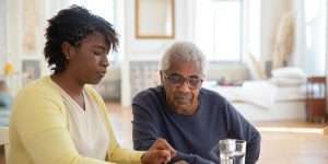 Adult daughter sitting at a kitchen table with her elderly father, talking through something together.