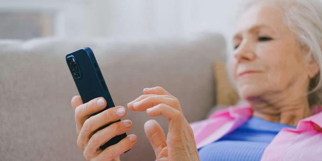 Older woman sitting on a sofa replying to a text message on her smartphone.